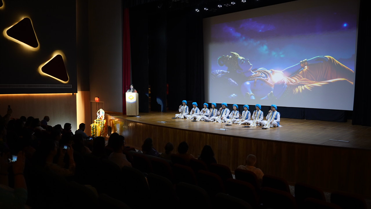 Audience attentively watching a presentation in a conference setting, with stage lights and speaker visible